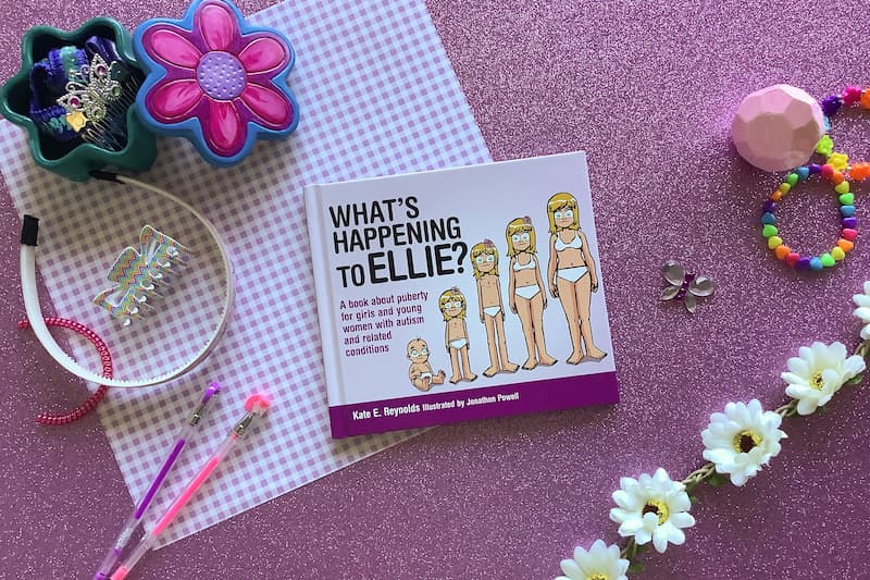 flat lay image of hardcover book 'what's happening to Ellie?' on a pink background surrounded by hair accessories, pens, and daisies